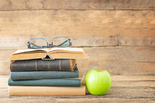 Back to school and education concept. Books, green apple and glasses on the open book on a wooden background and place for text. - Powered by Adobe