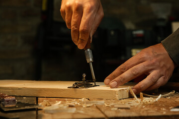 Carpenter screwing metal chrome hinges on wooden plank in the workshop.	