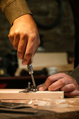 Carpenter screwing metal chrome hinges on wooden plank in the workshop.	