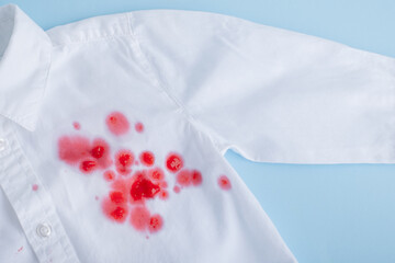 Obraz na płótnie Canvas Сlose up spill beverage on clothes. Bright pink stain on a white shirt from the front. isolated on blue background