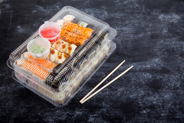 Two plastic boxes with sets of rolls, wasabi and ginger, bamboo chopsticks on a black background.