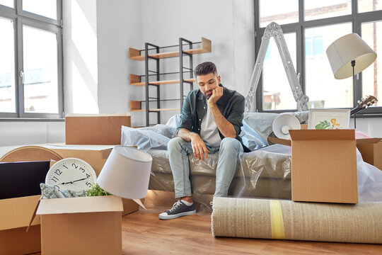 moving, eviction and real estate concept - sad man with boxes at new home