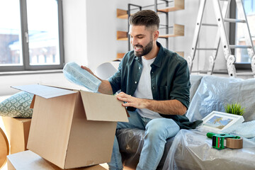 moving, people and real estate concept - happy smiling man unpacking boxes at new home