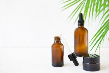 Glass bottles for care oils or serums with a branch of a palm tree on a white background. Summer face and body care concept.
