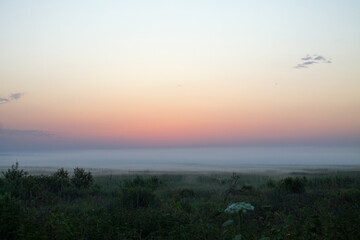 Dramatic landscape - early summer morning before sunrise on the horizon and fog over the meadow