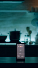 Phone with intelligent software placed on table in kitchen with nobody in, controlling light with high tech application. Mobile with smart home app in empty house automation system