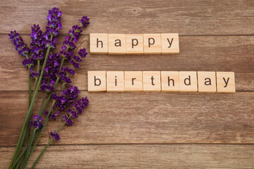 Happy birthday card design, with wooden tiles with letters and bunch of fresh blossoming lavender, isolated on rustic wooden background, high angle view