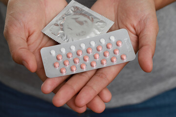 woman holding birth control pills and condoms in hand Take care of yourself and your family