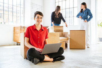 Young woman at laptop while moving home - Businesswoman working on portable device while setting up...