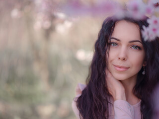 Naklejka premium A beautiful young woman near a blooming spring pink tree