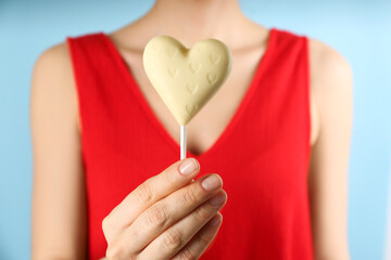 Woman holding heart shaped lollipop made of chocolate on light blue background, closeup