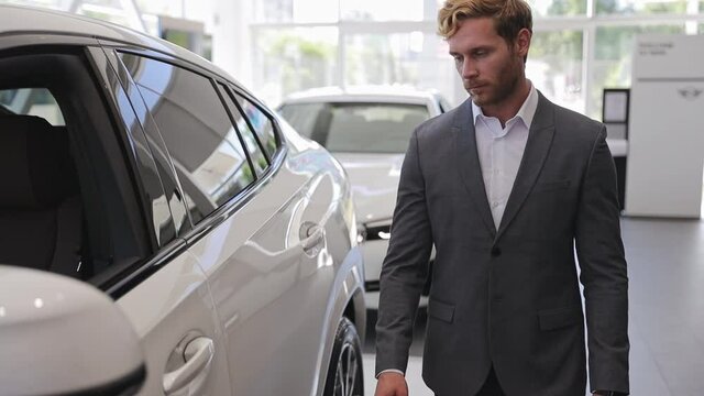 Happy adult man customer male buyer businessman client wears classic suit chooses auto wants to buy new automobile in car showroom vehicle salon dealership store motor show indoors. Car sales concept