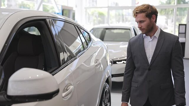 Happy adult man customer male buyer businessman client wears classic suit chooses auto wants to buy new automobile in car showroom vehicle salon dealership store motor show indoors. Car sales concept