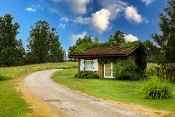 Fototapeta na wymiar small wooden lodge and country road in countryside. idyllic landscape