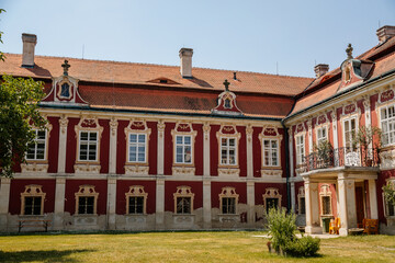 Naklejka premium Baroque castle Steknik, stucco, peeling dark red plaster, red tile roof, green lawn, italian garden, aristocratic residence in summer sunny day, ancient chateau Steknik, Czech Republic