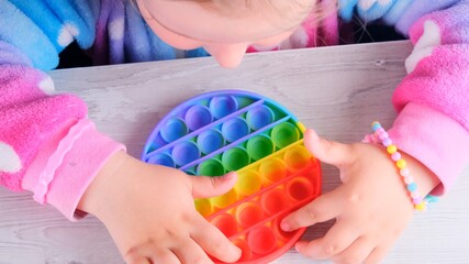 cute little girls playing with enthusiasm pop it sensory toy circle form. little female presses colorful rainbow squishy soft silicone bubbles on white background. Stress and anxiety relief. Trendy