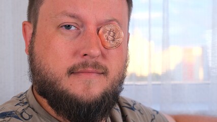 man holds bitcoins. Male with bitcoin in eye. Bitcoin is a cryptocurrency invented in 2008 by an unknown person or group of people using the name Satoshi Nakamoto.