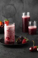 Different type glass with fresh berries smoothie and cherry, strawberry and raspberry fruit on dark background.