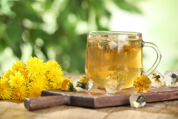 Delicious fresh tea, dandelion flowers and ice cubes on wooden table against blurred background