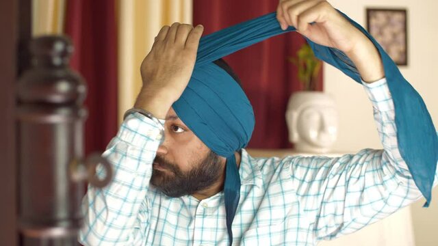 Portrait of a mature Sikh gentleman fixing his turban by pleating the ends. Medium shot of an Indian Punjabi man trying to adjust his turban properly while looking into the mirror