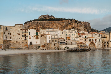 Fototapeta na wymiar Sunrise on beach in Cefalu, Sicily, Italy, old town panoramic view with colorful waterfront houses, sea and La Rocca cliff.Attractive summer cityscape,traveling concept background.Italian vacation.