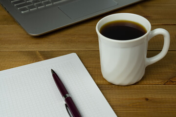 A cup of coffee and notebook for notes on the desktop. Coffee break and relax during work or study.