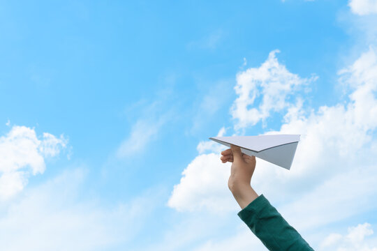 Child hand holding paper airplane on blue sky background with white clouds. Copy space. - Powered by Adobe
