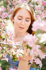 Fototapeta premium Close-up gentle portrait of a red-haired girl around her pink flowers from a cherry tree and an apple tree. Clean skin and youth concept.