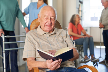 Senior man is sitting in an armchair and reading a book relaxed