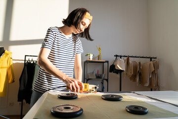Professional young female tailor making clothing samples in factory or design studio with electric...