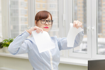 young pretty business woman in strict stylish clothes and glasses in the office near the desktop tearing documents