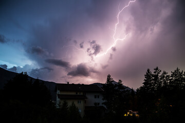 Blitze über einem Haus zwischen Bäumen