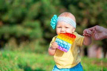 A little 8-month-old girl in a yellow T-shirt holds an eternal bubble in her mouth, leaning on her mother's hand. Simple dimple. The toy is anti-stress.