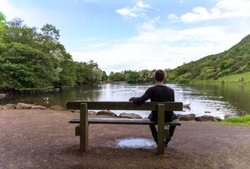 young lonely man seated on a bench near a lake