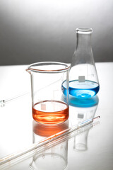 Vertical image of two glassware and red,blue laboratory liquids in it, glass pipette on the lab table