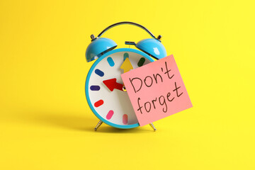Alarm clock and reminder note with phrase Don't forget on yellow background - obrazy, fototapety, plakaty