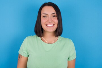 young beautiful brunette girl with short hair standing against blue background with a happy and cool smile on face. Lucky person.