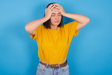 young beautiful brunette girl with short hair standing against blue background suffering from...