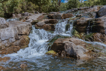 Selective focus close-up of clear stream water running over large rocks. Water running through a parkland during the daytime. Water runs through the stones summer time