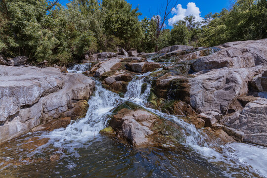 Selective focus close-up of clear stream water running over large rocks. Water running through a parkland during the daytime. Water runs through the stones summer time