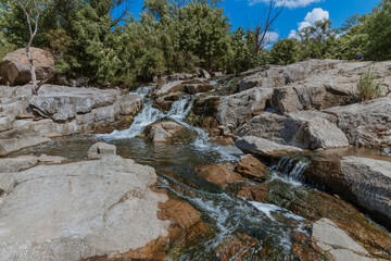 Selective focus close-up of clear stream water running over large rocks. Water running through a parkland during the daytime. Water runs through the stones summer time