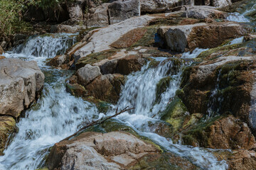 Fototapeta na wymiar Selective focus close-up of clear stream water running over large rocks. Water running through a parkland during the daytime. Water runs through the stones summer time