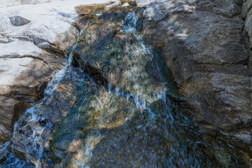 Selective focus close-up of clear stream water running over large rocks. Water running through a parkland during the daytime. Water runs through the stones summer time