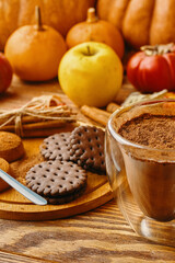 Obraz na płótnie Canvas Hot cocoa, cookies and autumn harvest on wooden table. Ripe pumpkins, apples, fall leaves and persimmons on background. Coffee with chocolate chips. Concept of Christmas, Thanksgiving and Halloween.