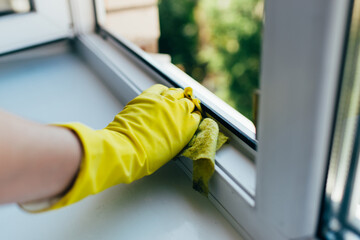 A person wearing gloves washes the window frame with a cleaning cloth