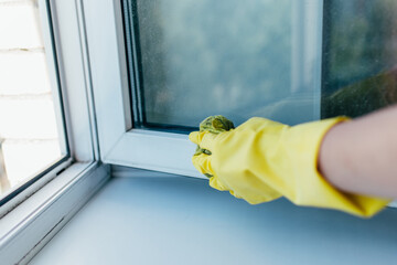 Cleaning service with gloves washes the window frame with a rag in the summer
