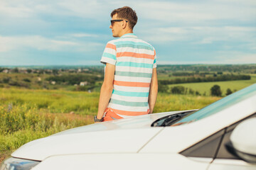 Fototapeta na wymiar Young male enjoying the beautiful landscape while driving his car, a man standing near his car