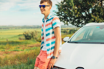 Young male enjoying the beautiful landscape while driving his car, a man standing near his car