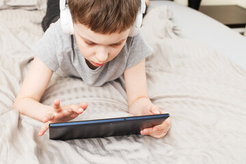 child boy lying on bed with pc tablet with wireless headphones
