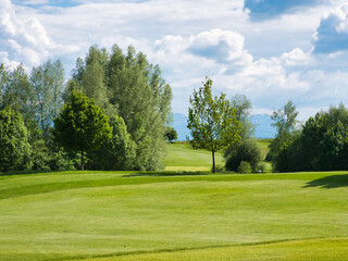 Fototapeta na wymiar Landscape with fairway of golf course and trees on sunny day with clouds